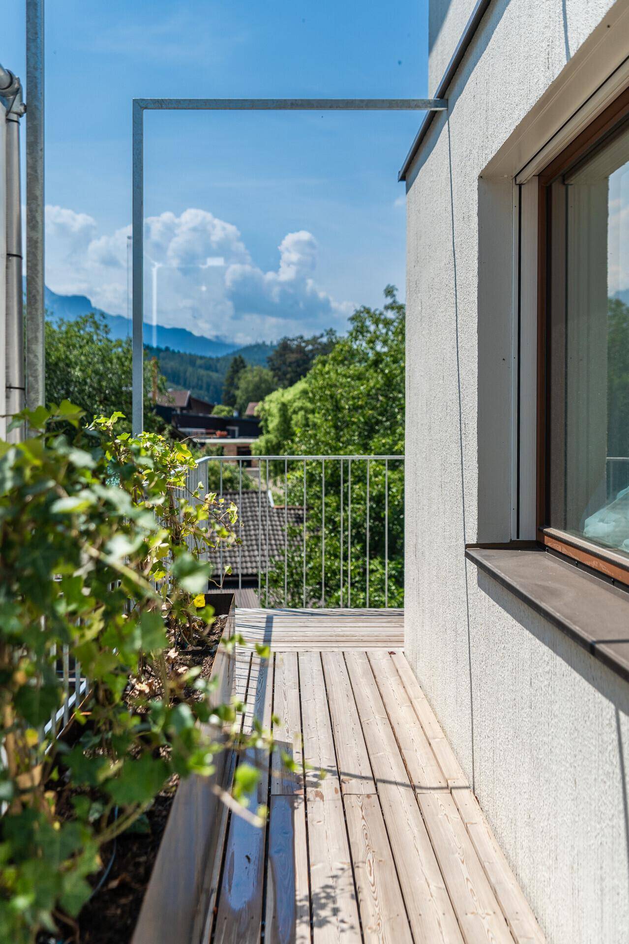 Schmaler Holzbalkon mit Metallgeländer und Blick auf die umliegende Natur und Häuser.