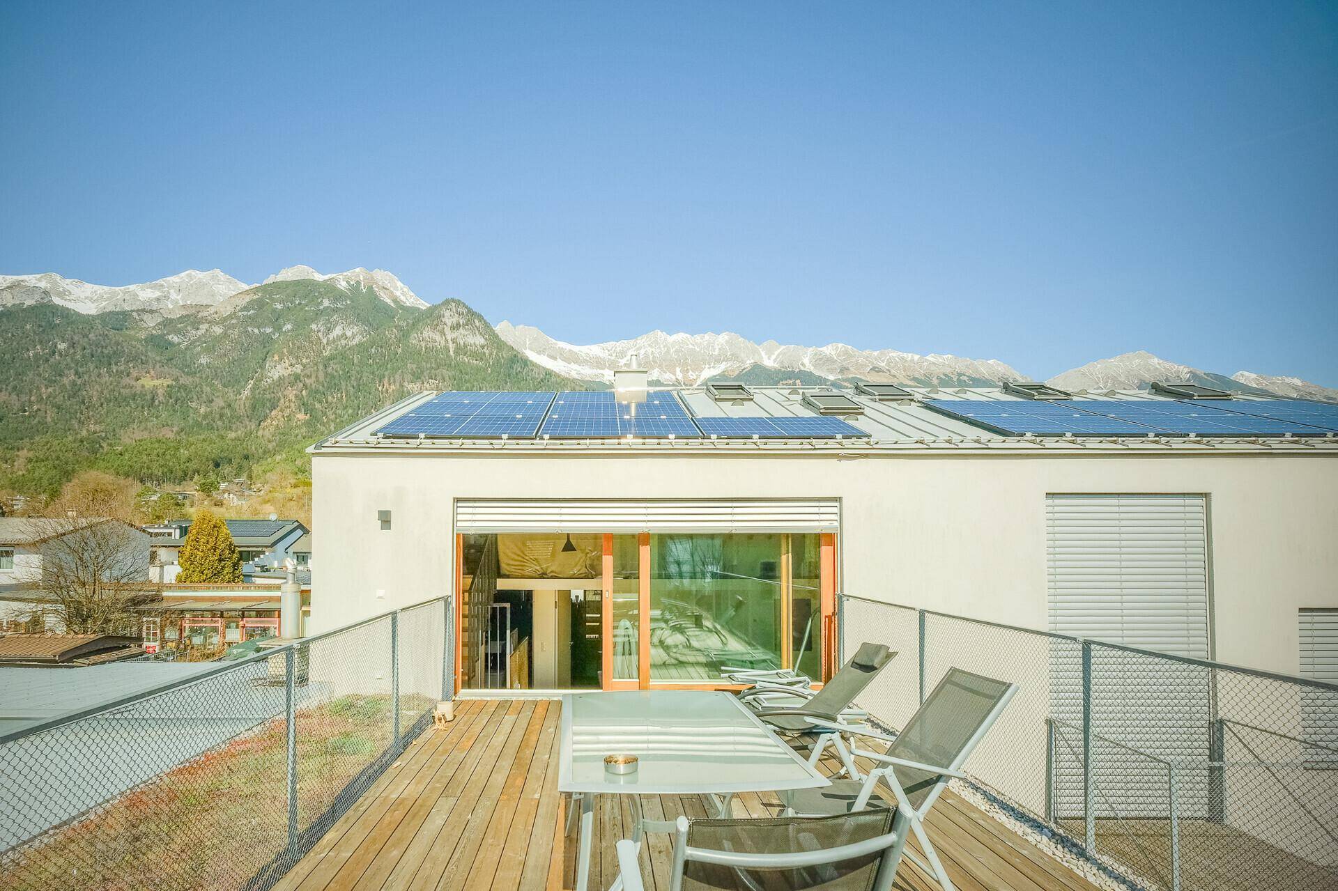 Sonnige Dachterrasse mit Holzboden, Gartenmöbeln und beeindruckendem Bergblick.