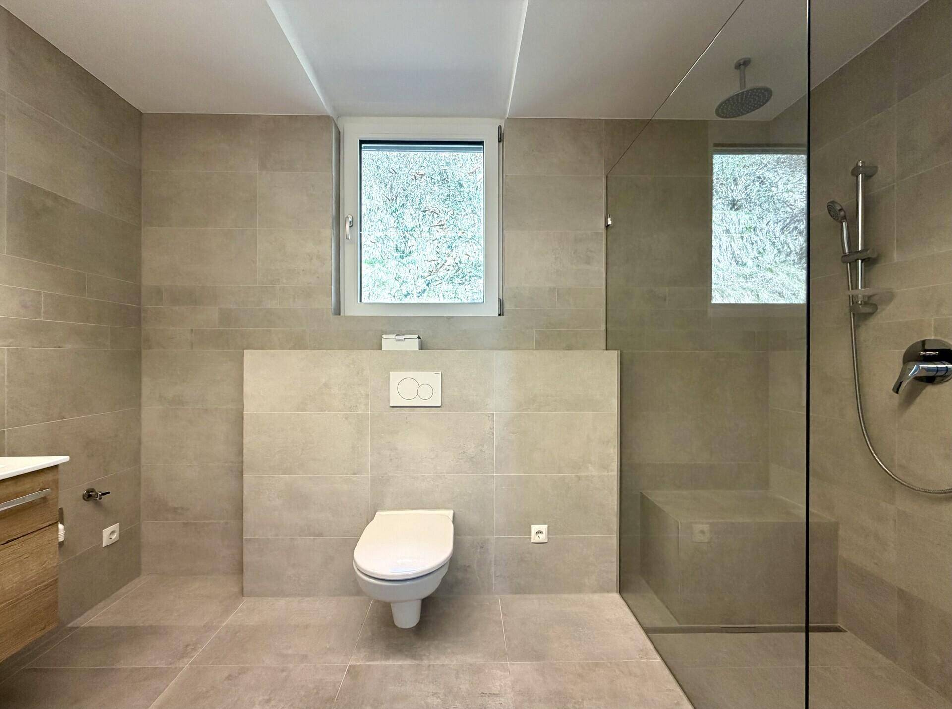 Modernes Badezimmer mit beigefarbenen Fliesen, bodengleicher Dusche und Fenster.