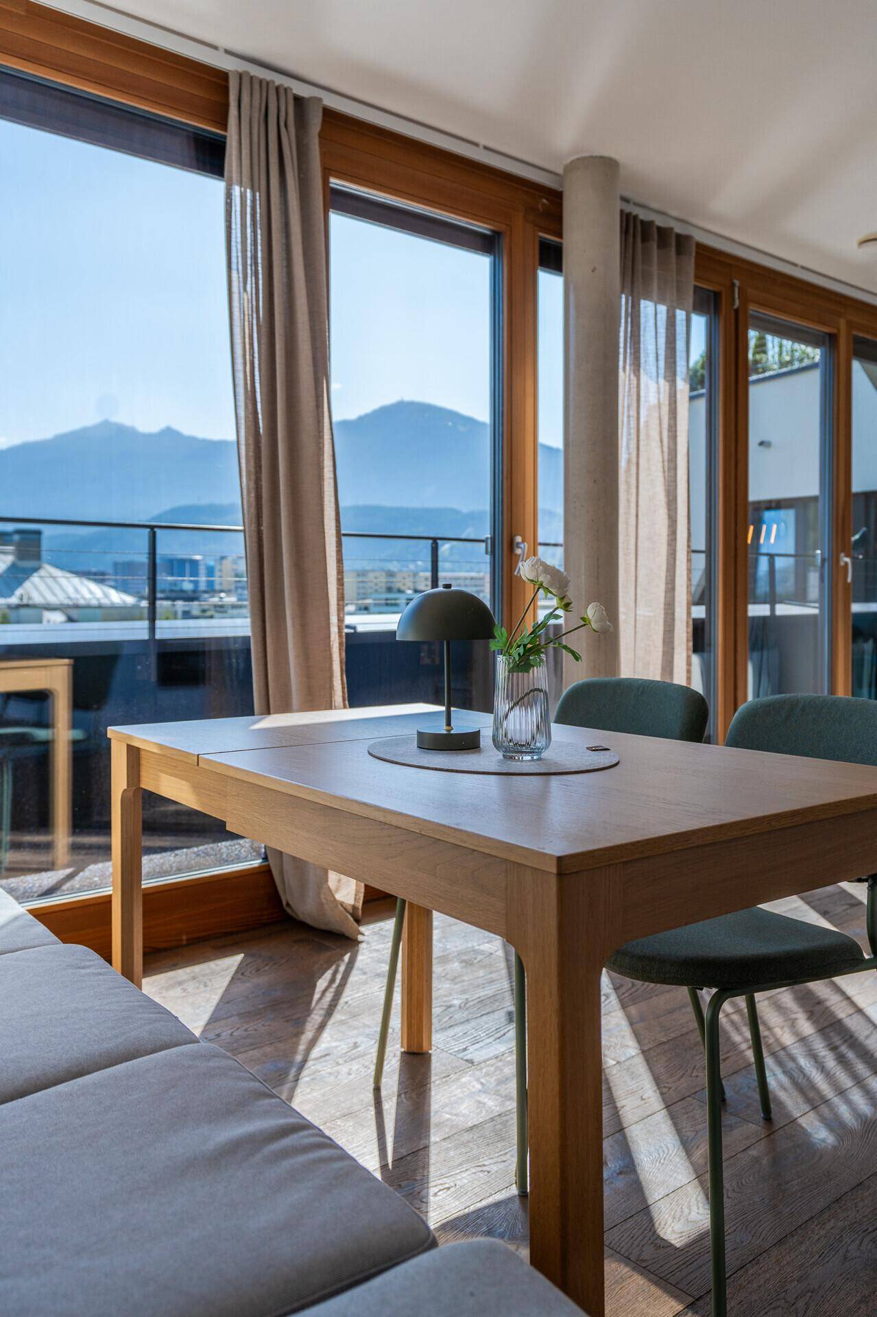 Heller Essbereich mit Holztisch und Stühlen, umgeben von großen Fenstern mit Bergblick.
