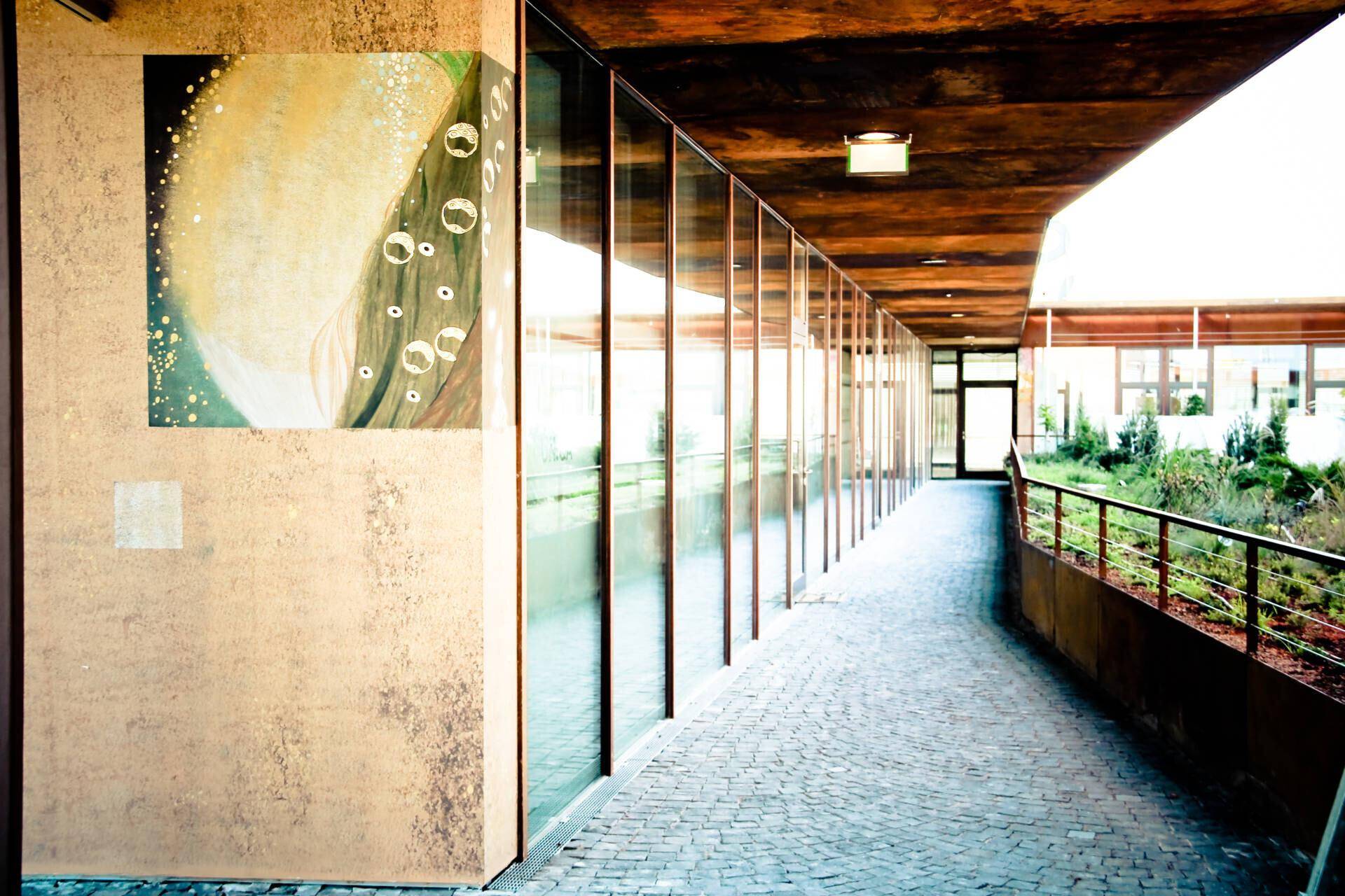 Langer, überdachter Außenflur mit Glaswänden und Kunst an der Wand.