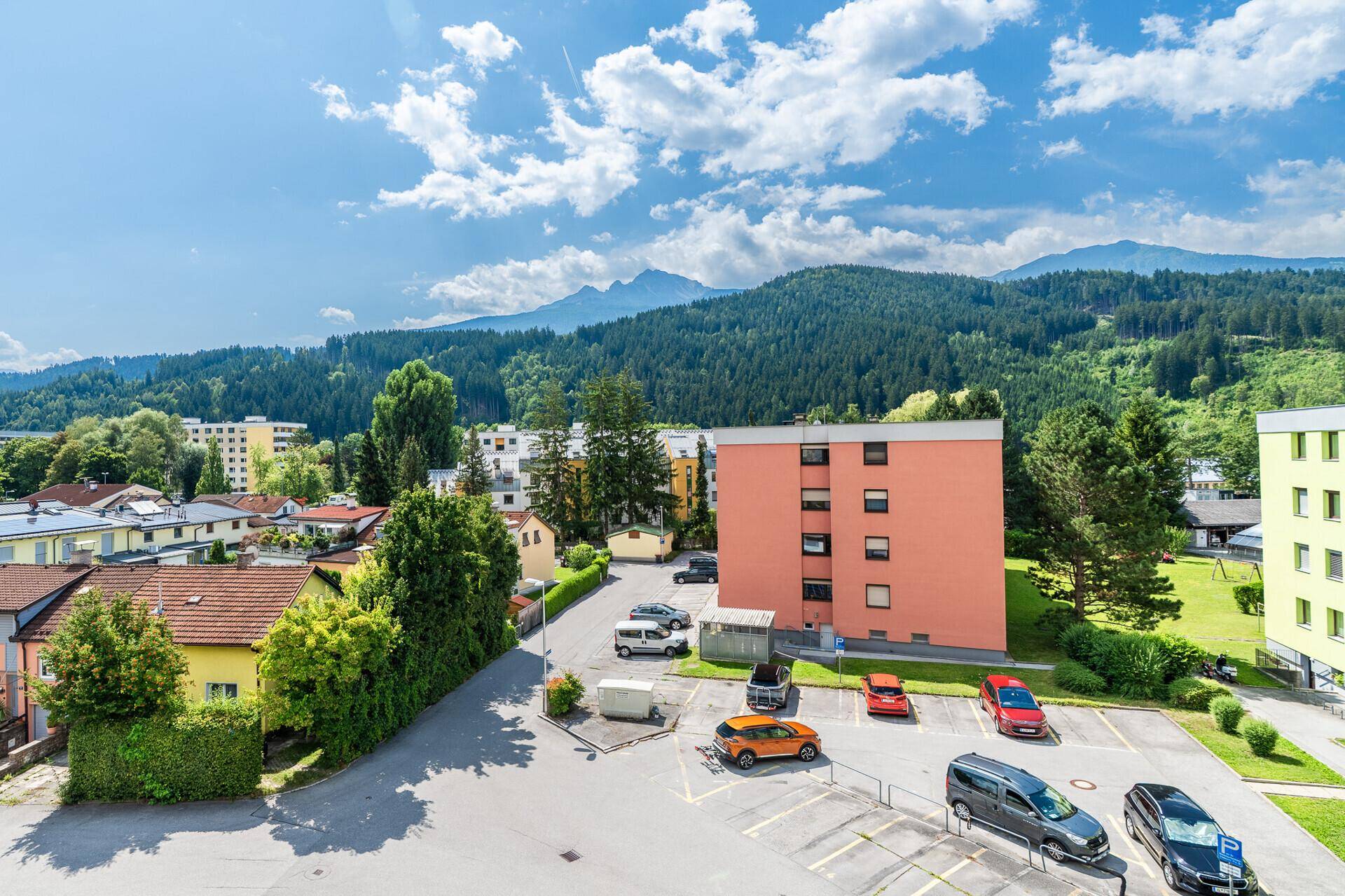 Panoramablick über eine Wohnsiedlung mit Parkplätzen und majestätischen Bergen im Hintergrund.