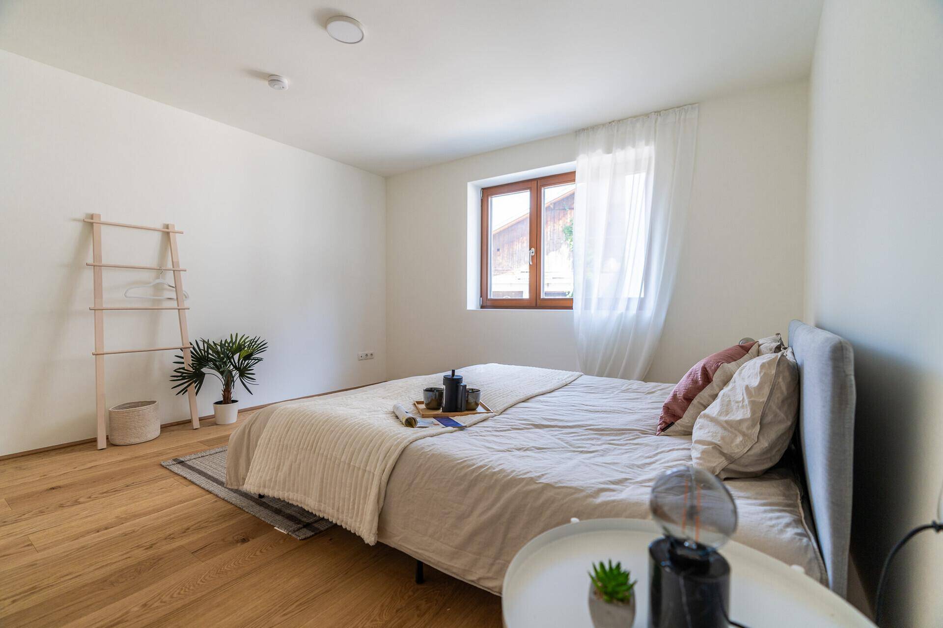 Helles Schlafzimmer mit Holzboden, großem Bett und einem Fenster, das viel natürliches Licht hereinlässt.