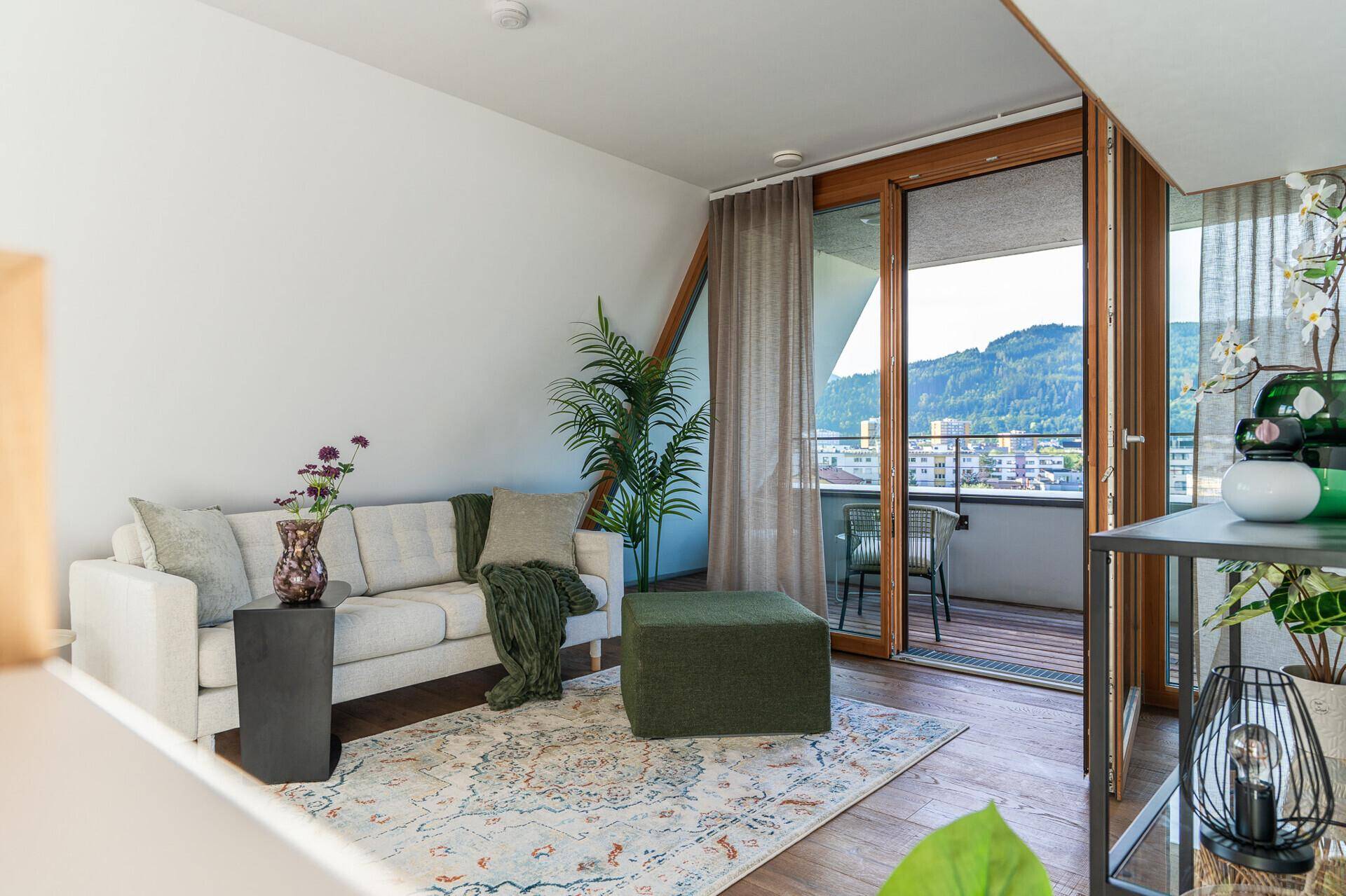 Gemütliches Wohnzimmer mit Sofa, Teppich und direktem Zugang zum Balkon mit Stadtblick.