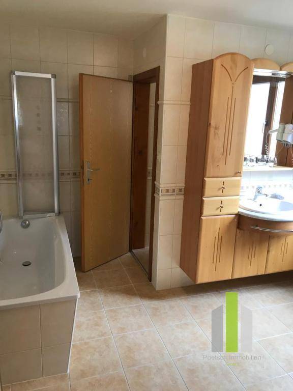 Helles Badezimmer mit Badewanne, Holzschrank und beigefarbenen Fliesen.