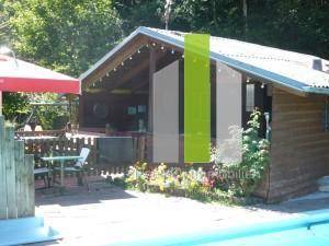 Holzverkleidetes Poolhaus mit überdachtem Sitzbereich und Blick auf den Pool.
