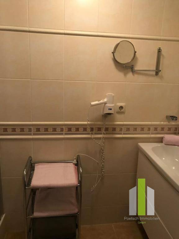 Badezimmer mit beigefarbenen Fliesen, Wandspiegel und Föhn an der Wand.