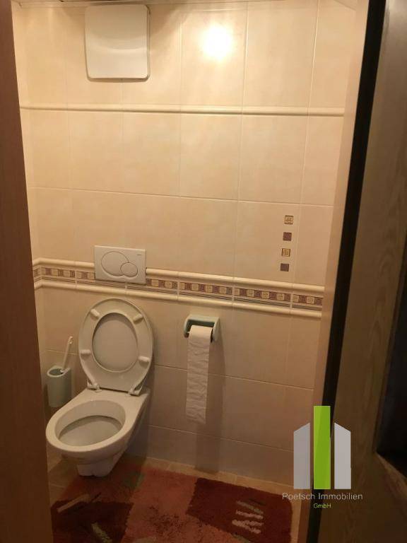 Kleines WC mit beigefarbenen Fliesen, Wand-WC und Spülkasten.