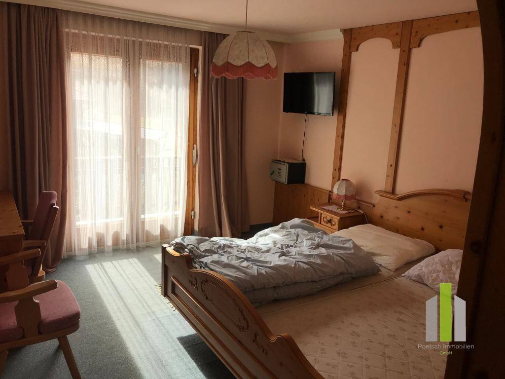 Gemütliches Schlafzimmer mit traditionellen Holzmöbeln, Teppichboden und viel Tageslicht durch die Balkontür.