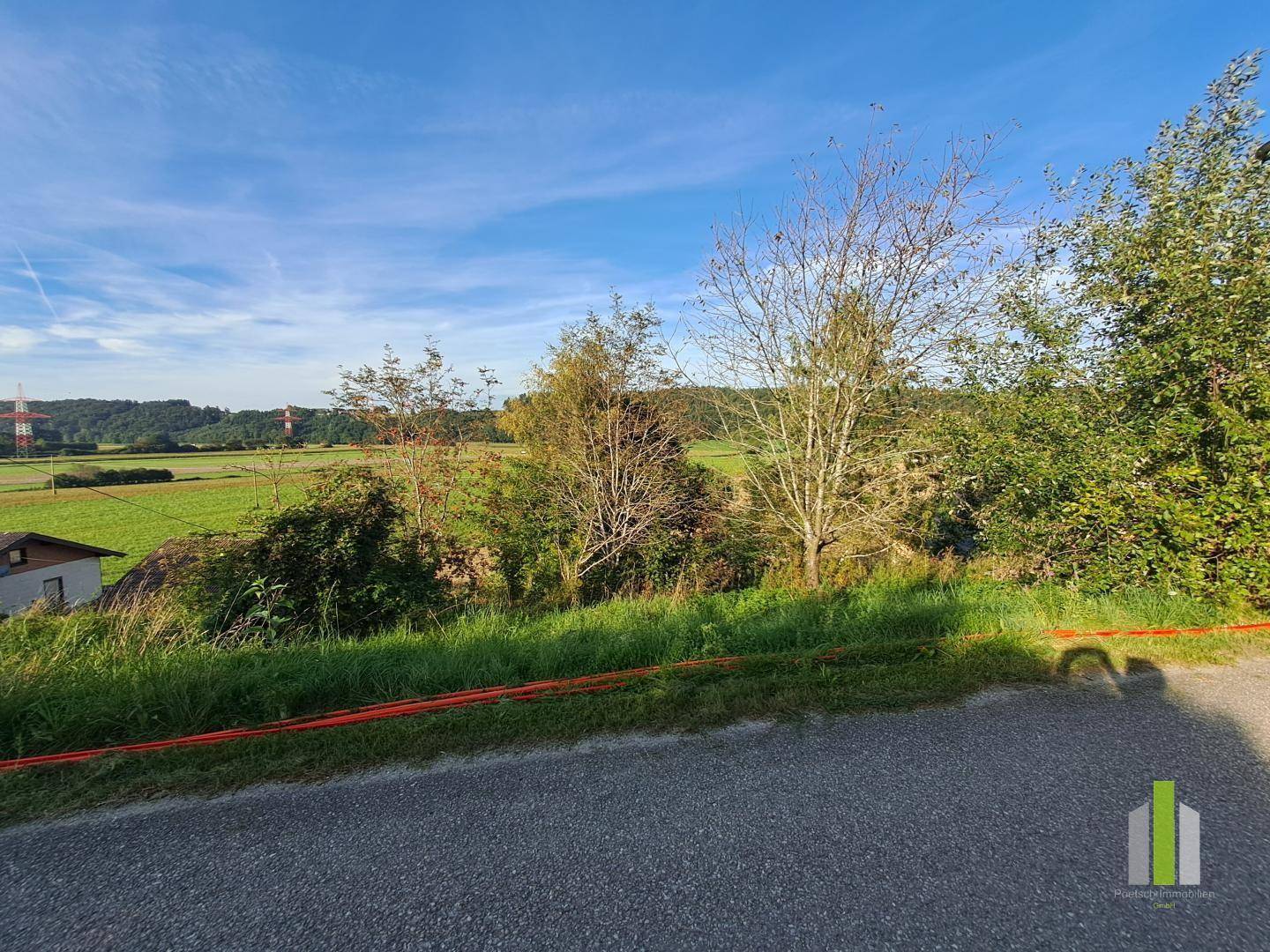 Blick auf weite Felder und grüne Hügel in ländlicher Umgebung unter blauem Himmel.