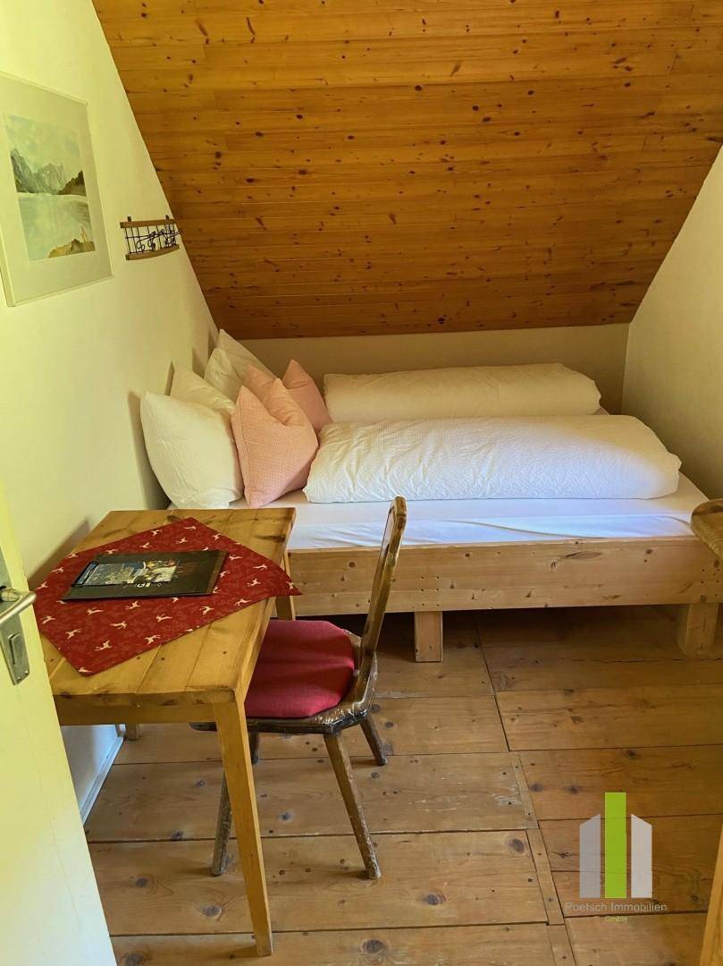 Dachgeschoss-Schlafzimmer mit Holzwänden, Holzboden und schräger Decke.