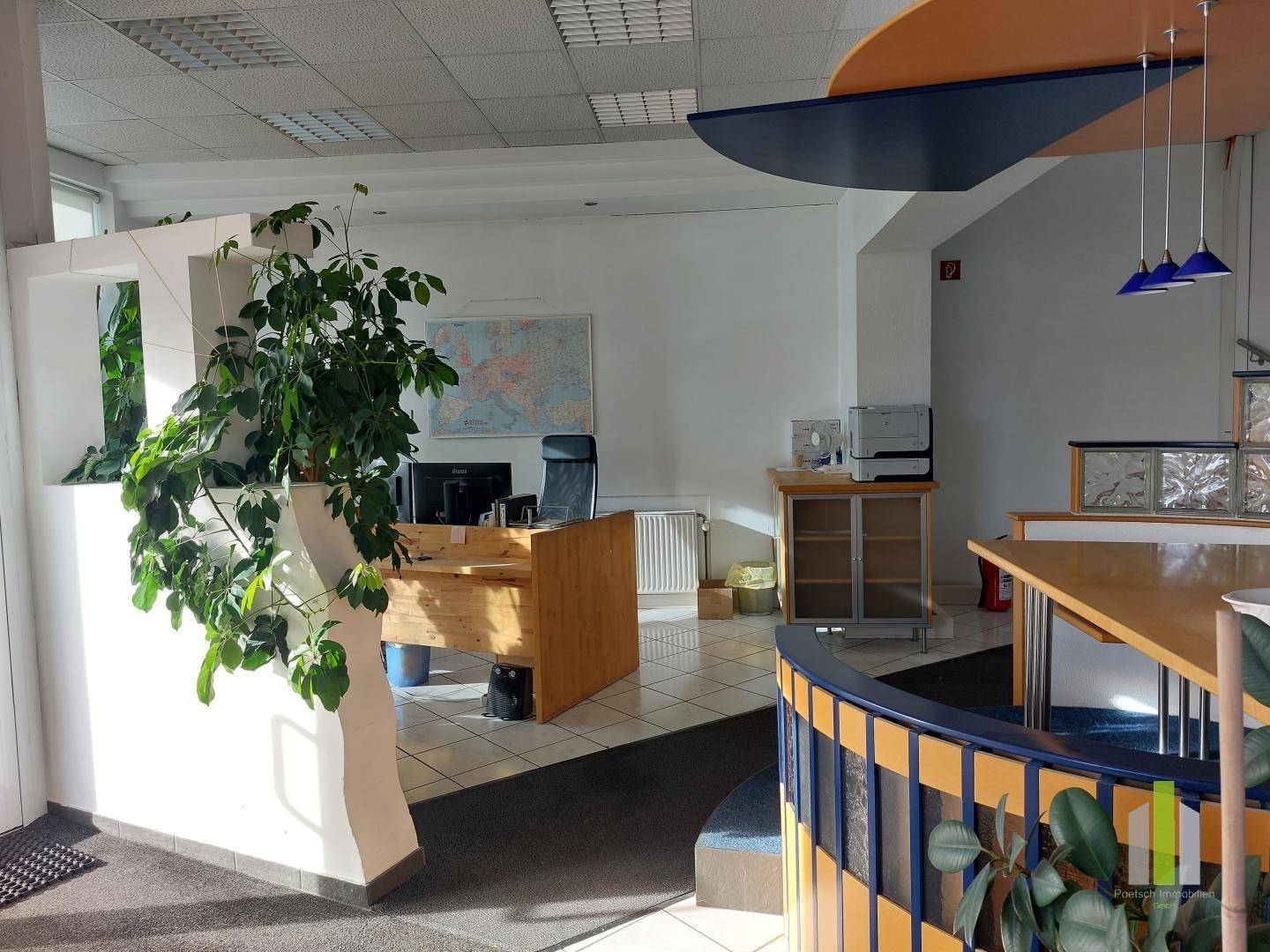 Heller Büroraum mit einem Holztisch, Bürostuhl und einer Weltkarte an der Wand, gut beleuchtet.