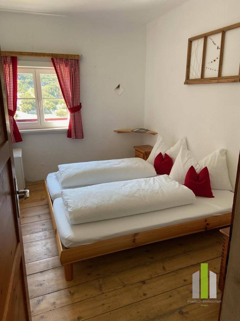 Einfaches Schlafzimmer mit zwei Einzelbetten, Holzdielenboden und Fenster mit rotem Vorhang.