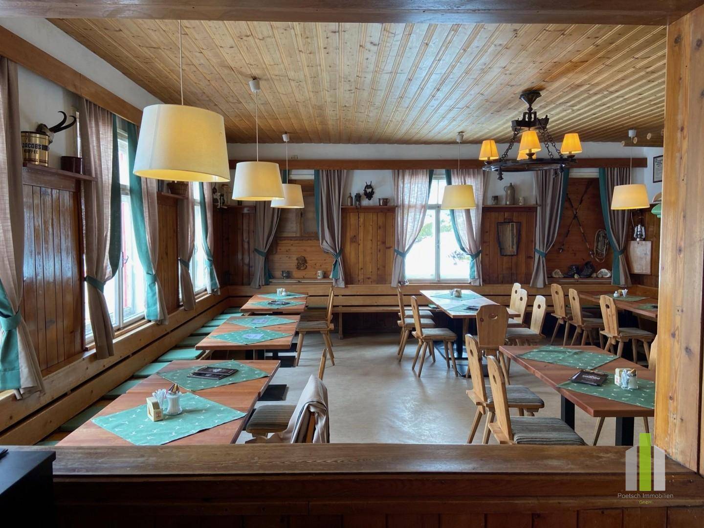 Traditioneller Speisesaal mit Holztäfelung, mehreren Tischen und gemütlicher Beleuchtung durch Hängelampen.