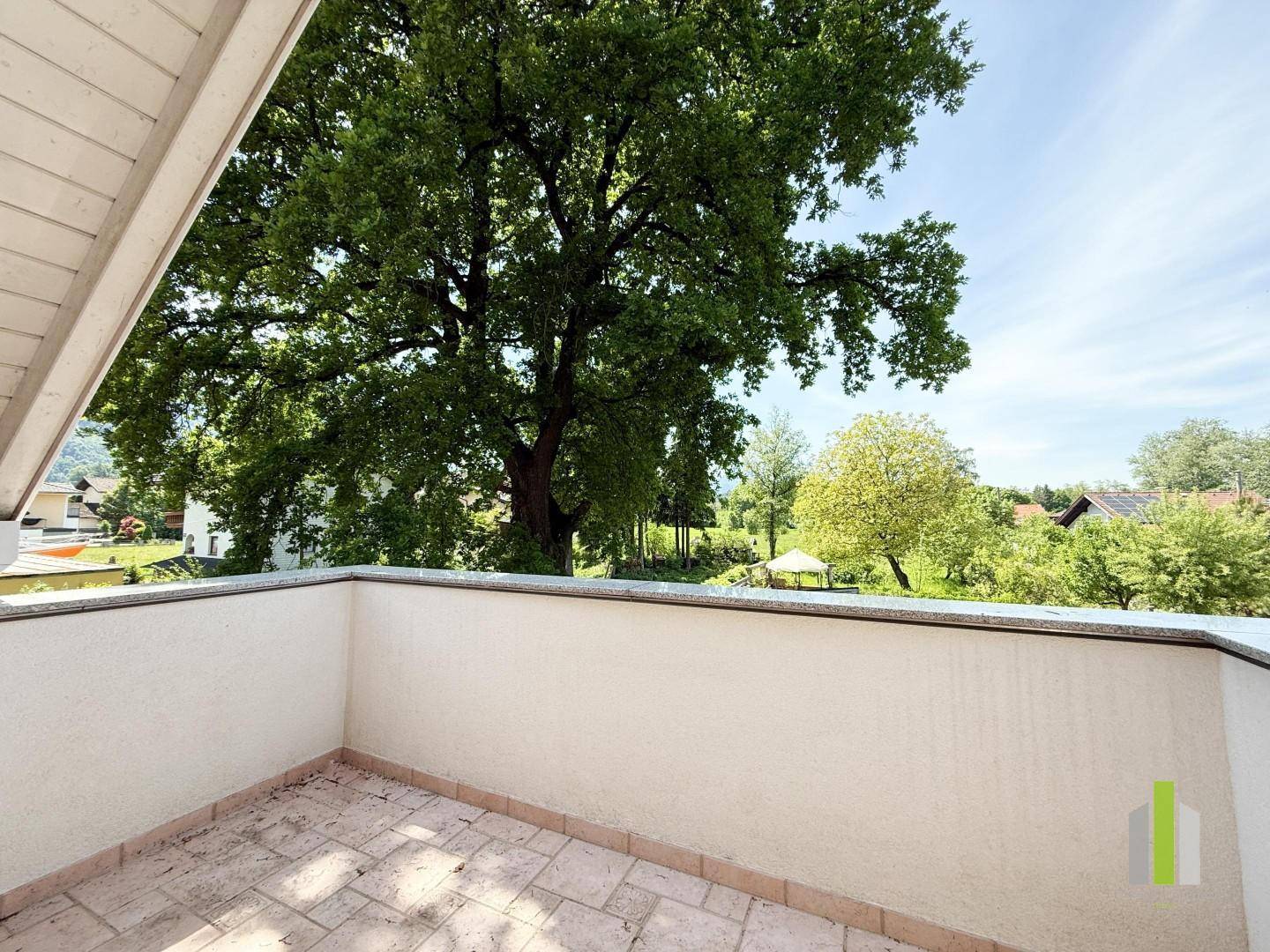 Geräumiger Balkon mit Fliesenboden und weitem Blick ins Grüne, umgeben von hohen Bäumen.