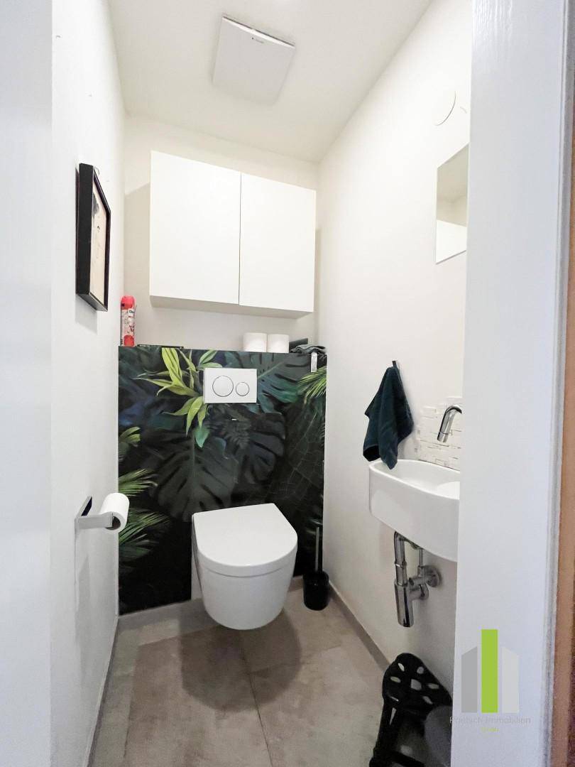 Kompakte Gästetoilette mit wandhängendem WC und dekorativer tropischer Tapete.