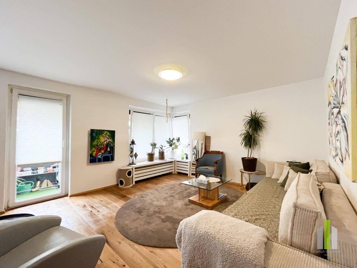 Lichtdurchflutetes Wohnzimmer mit Holzboden, gemütlichem Sofa und Zugang zu einem Außenbereich.