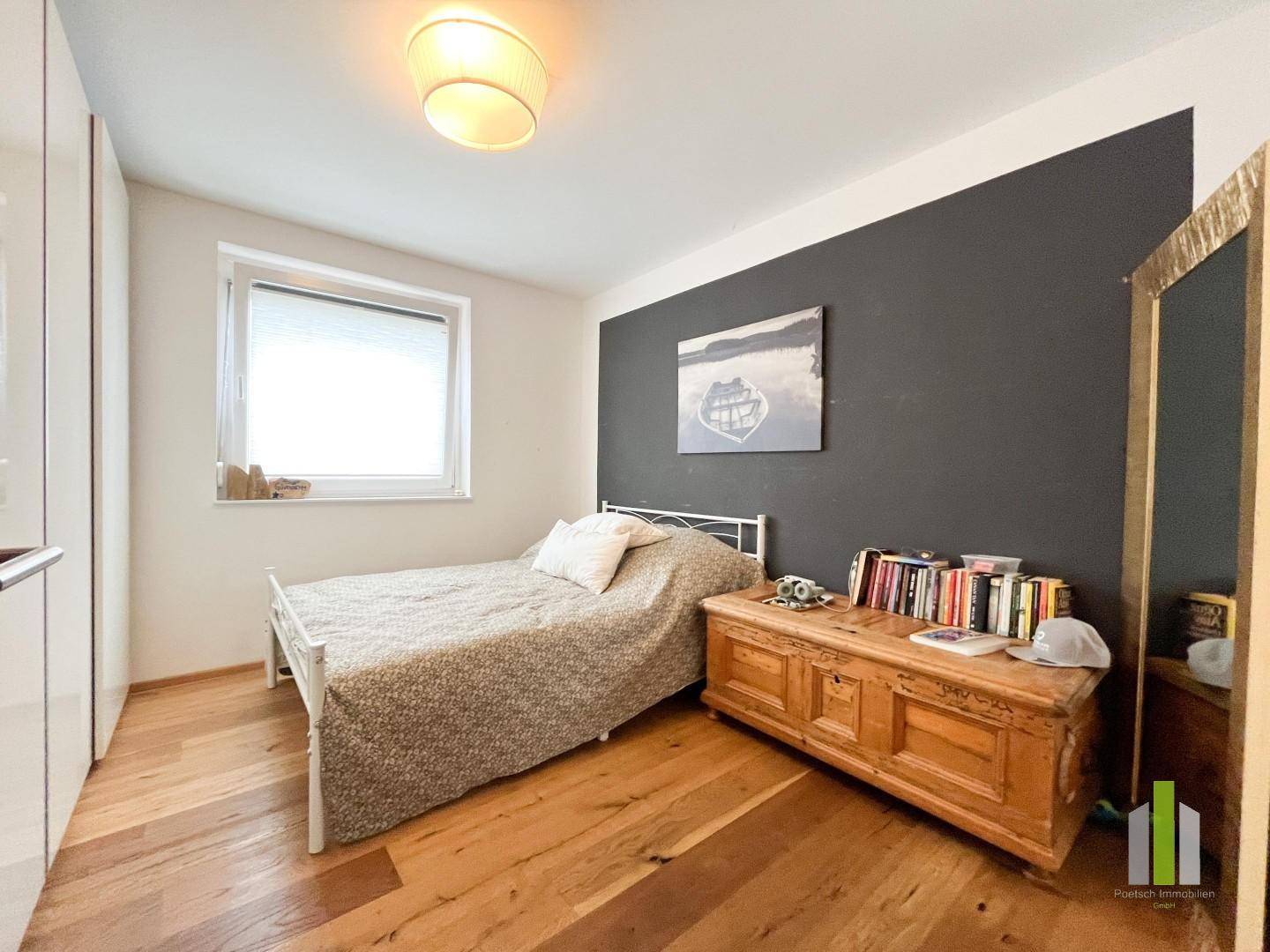 Schlafzimmer mit Einzelbett, Holzboden und einer dunklen Akzentwand für einen modernen Touch.