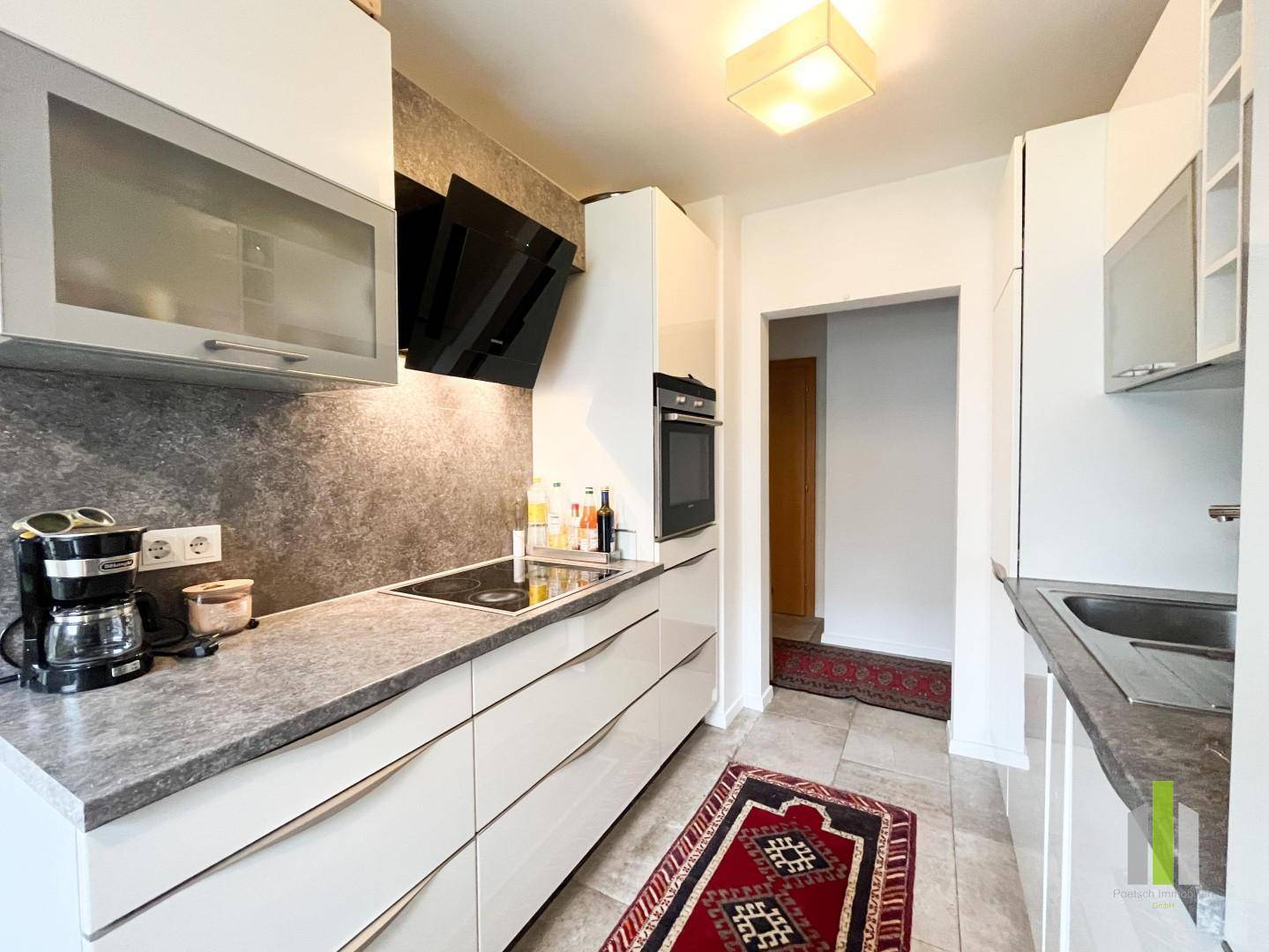Moderne Einbauküche mit weißen Hochglanzfronten, grauer Arbeitsplatte und integrierten Geräten.