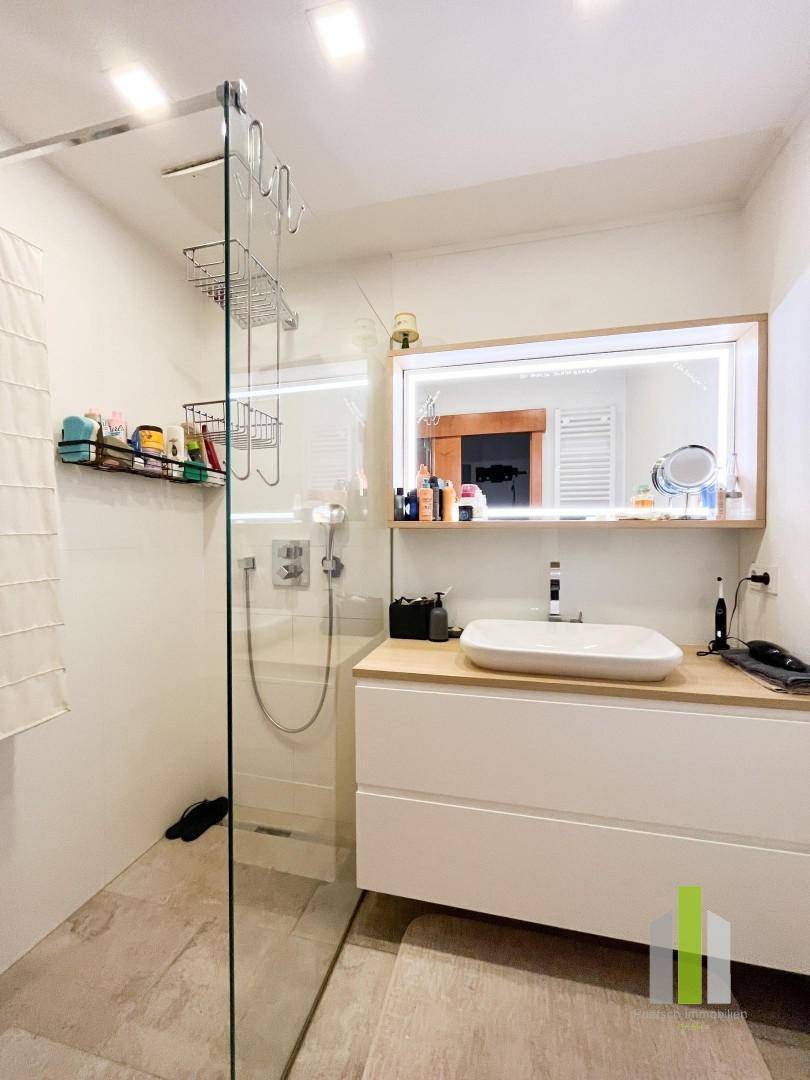 Modernes Badezimmer mit ebenerdiger Dusche, Einzelwaschbecken und beleuchtetem Spiegelschrank.