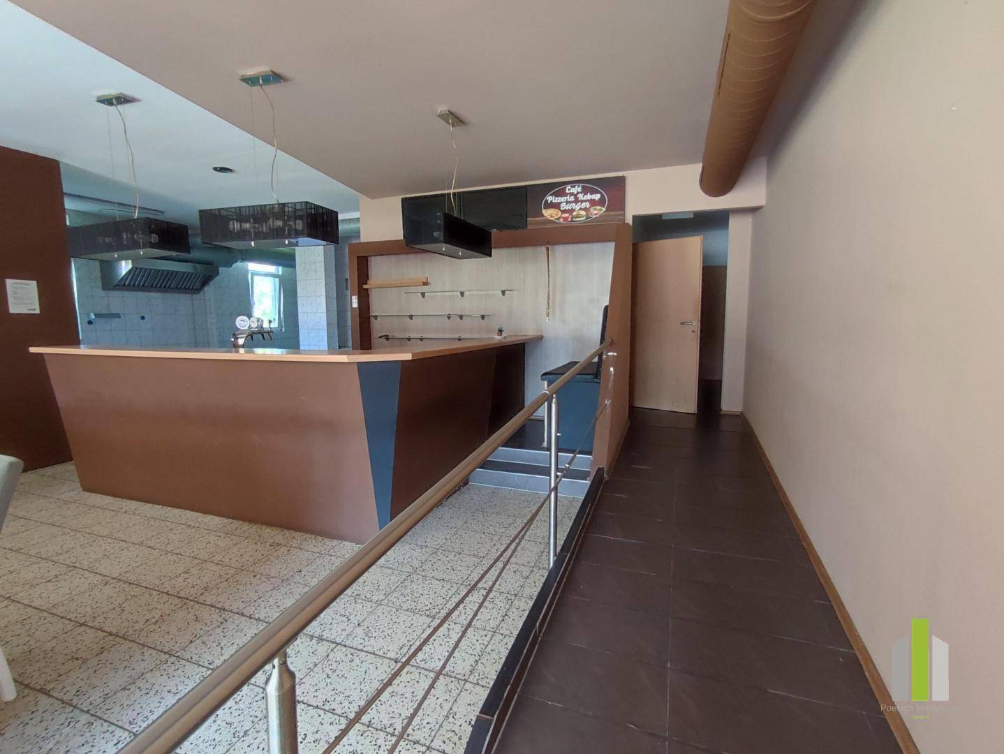 Eingangsbereich eines Restaurants mit Rampe, Theke und Blick in den Küchenbereich im Hintergrund.