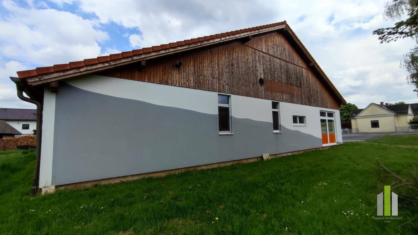 Rückseite eines Gebäudes mit Holzverkleidung im oberen Bereich und einer modern gestalteten Fassade.