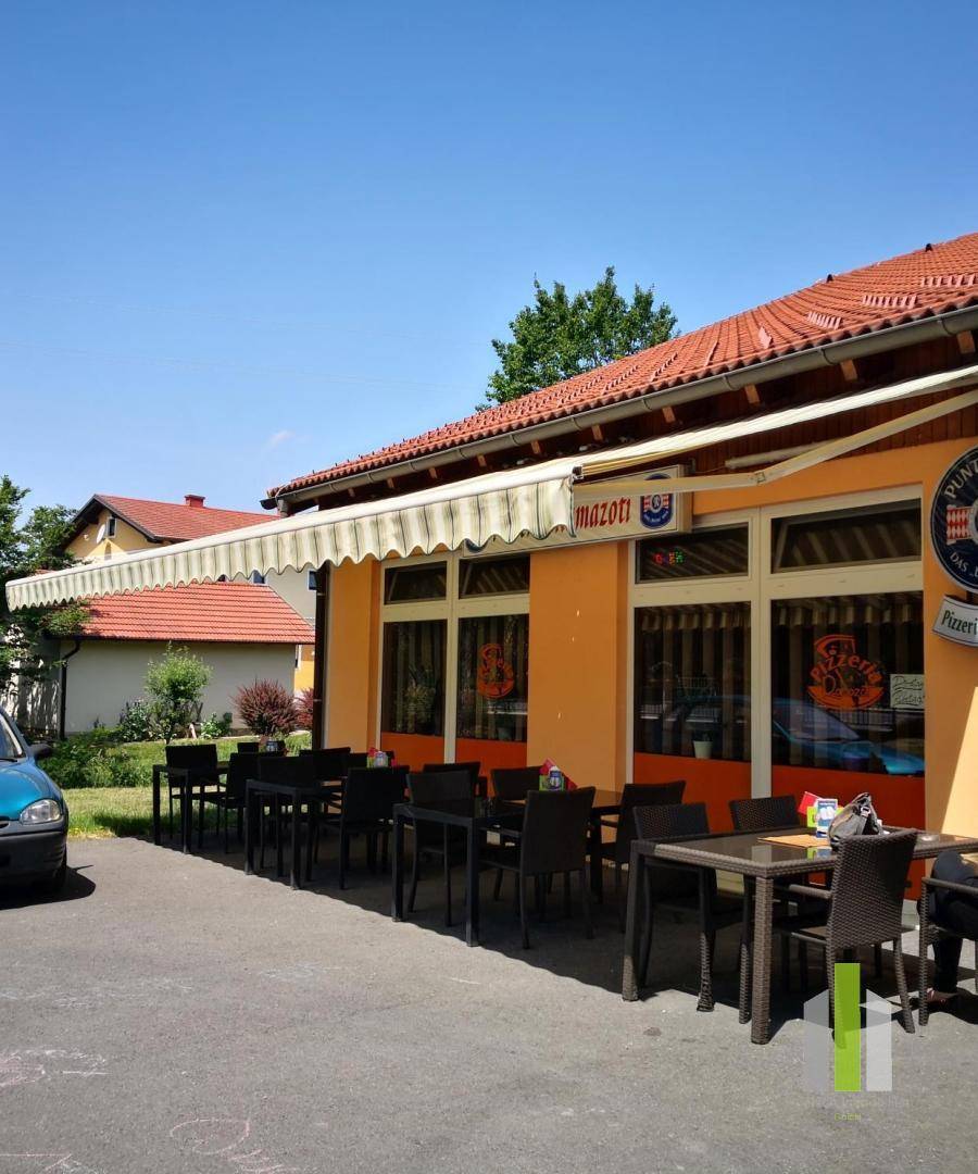 Außenterrasse eines Restaurants mit Tischen, Stühlen und einer Markise unter blauem Himmel.