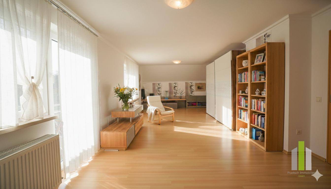 Heller Wohnraum mit Holzfußboden, großen Fenstern und einem Bücherregal an der Wand.
