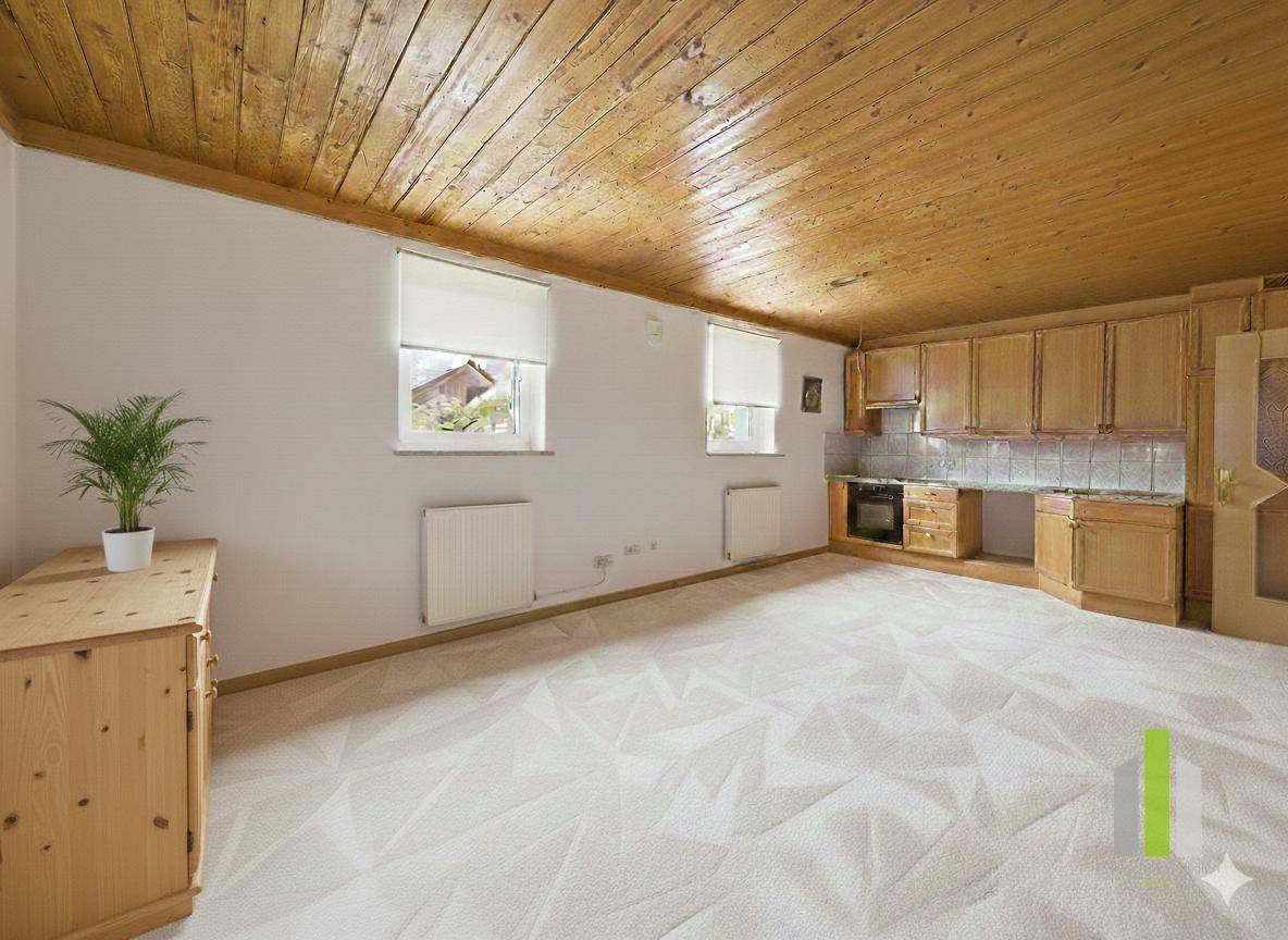 Gemütlicher Raum mit Teppichboden, Holzdecke und einer kleinen Küchenzeile.