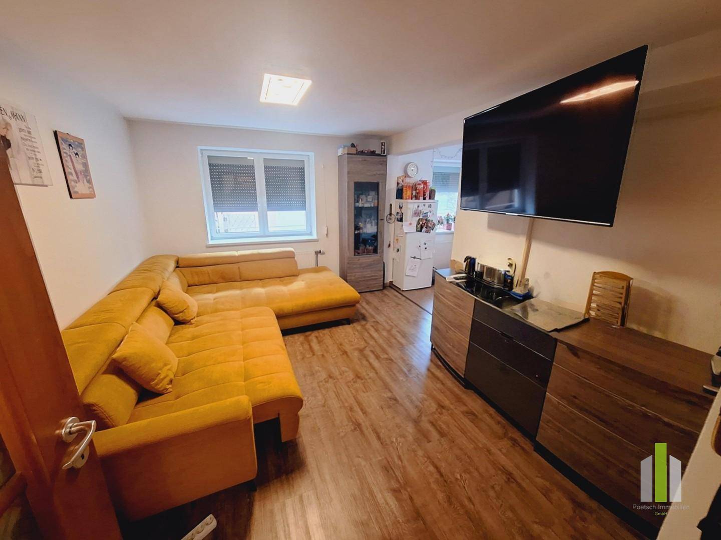 Offener Wohnbereich mit Sofa, großem Fernseher und Blick in die angrenzende Küche.