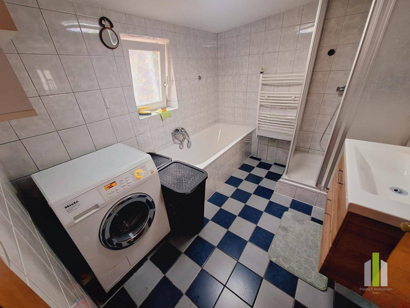 Badezimmer mit Badewanne, Duschkabine, Waschmaschine und einem Fenster, gefliest in Hellblau und Weiß.