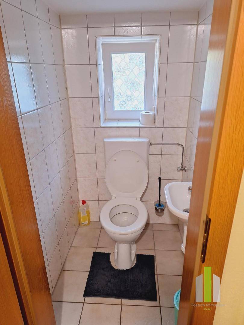 Kleines Gäste-WC mit Toilette, Waschbecken und einem Fenster, komplett gefliest.