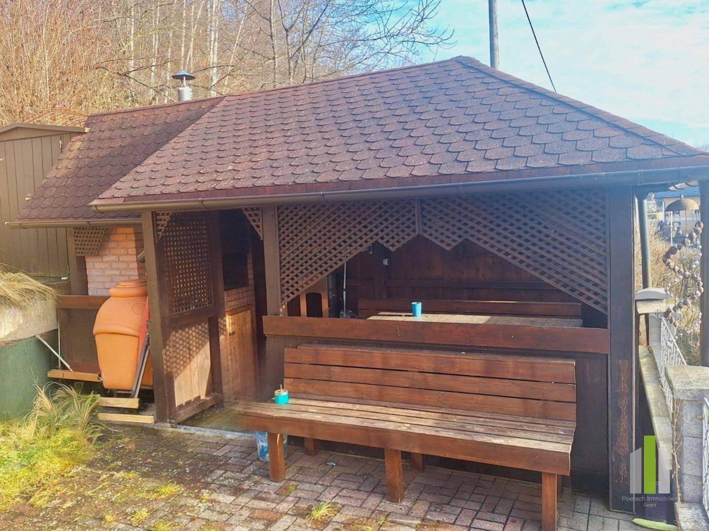 Rustikaler Holzpavillon mit integrierten Sitzbänken und einem Grillbereich, ideal für gesellige Stunden.