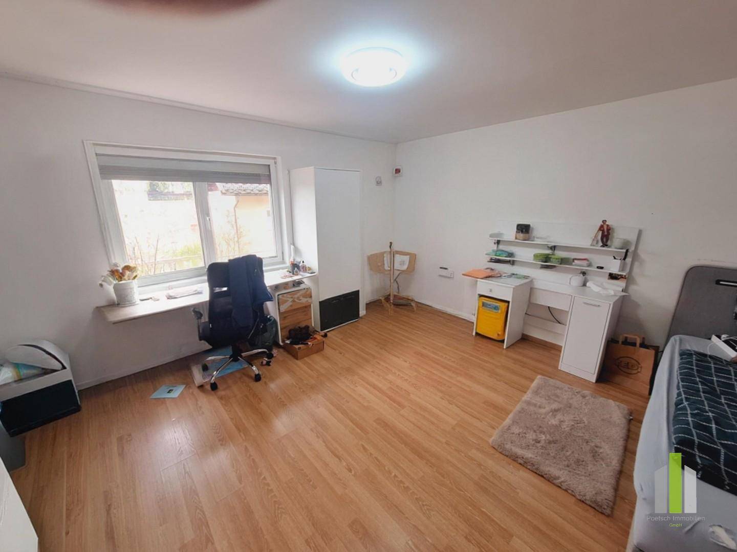 Geräumiges Arbeitszimmer mit Schreibtisch, Bürostuhl und einem großen Fenster für natürliche Beleuchtung.