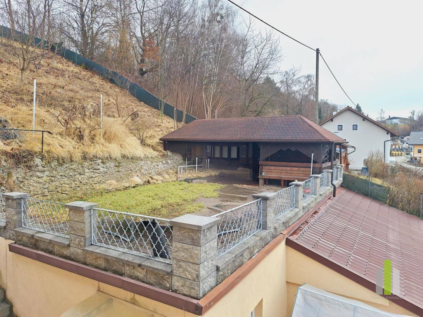 Gartenbereich mit einer kleinen Rasenfläche und einem überdachten Holzpavillon am Hang.