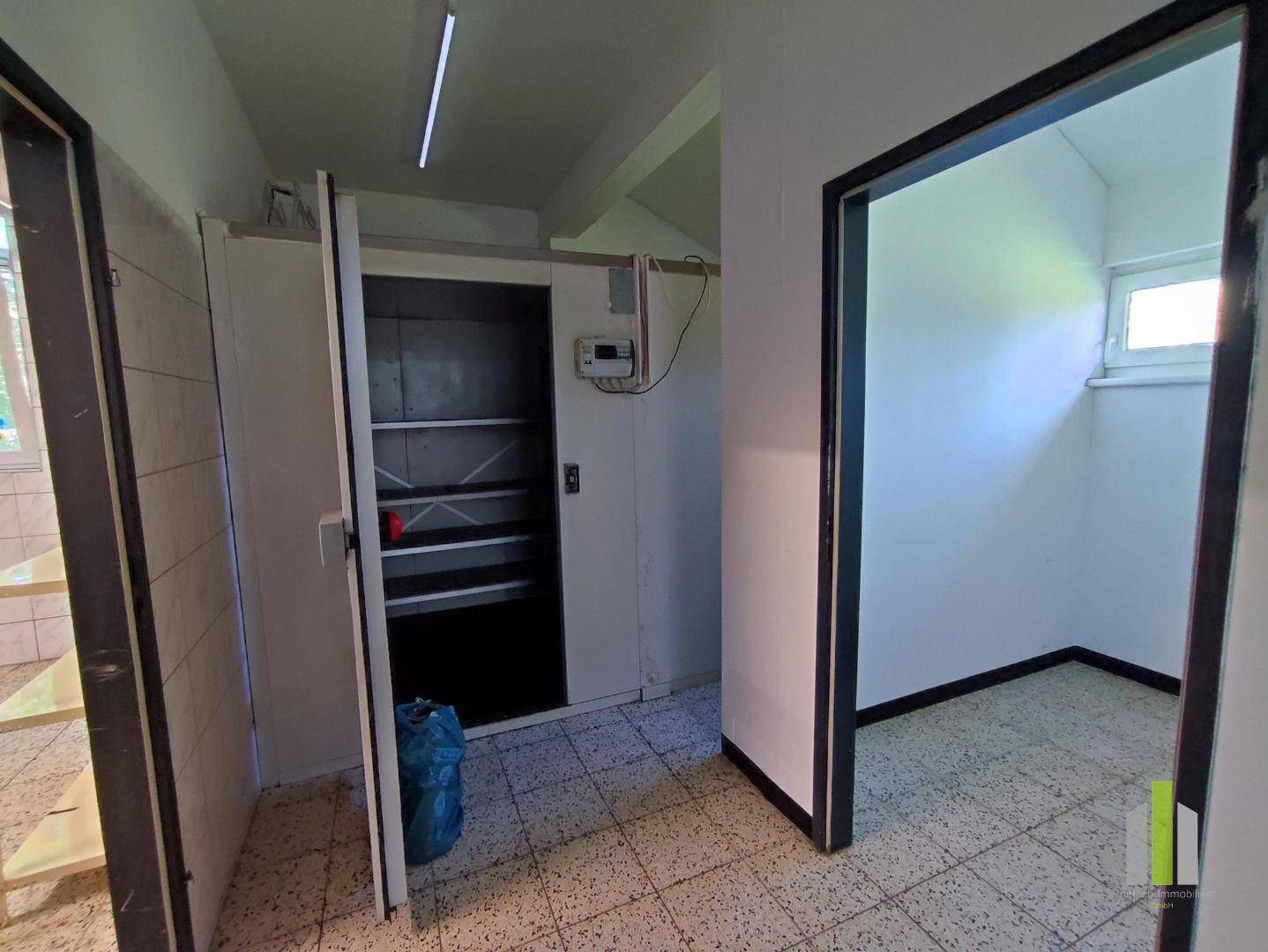 Lagerraum mit Regalen und einem Aufzug, daneben ein weiterer Raum mit Fenster.