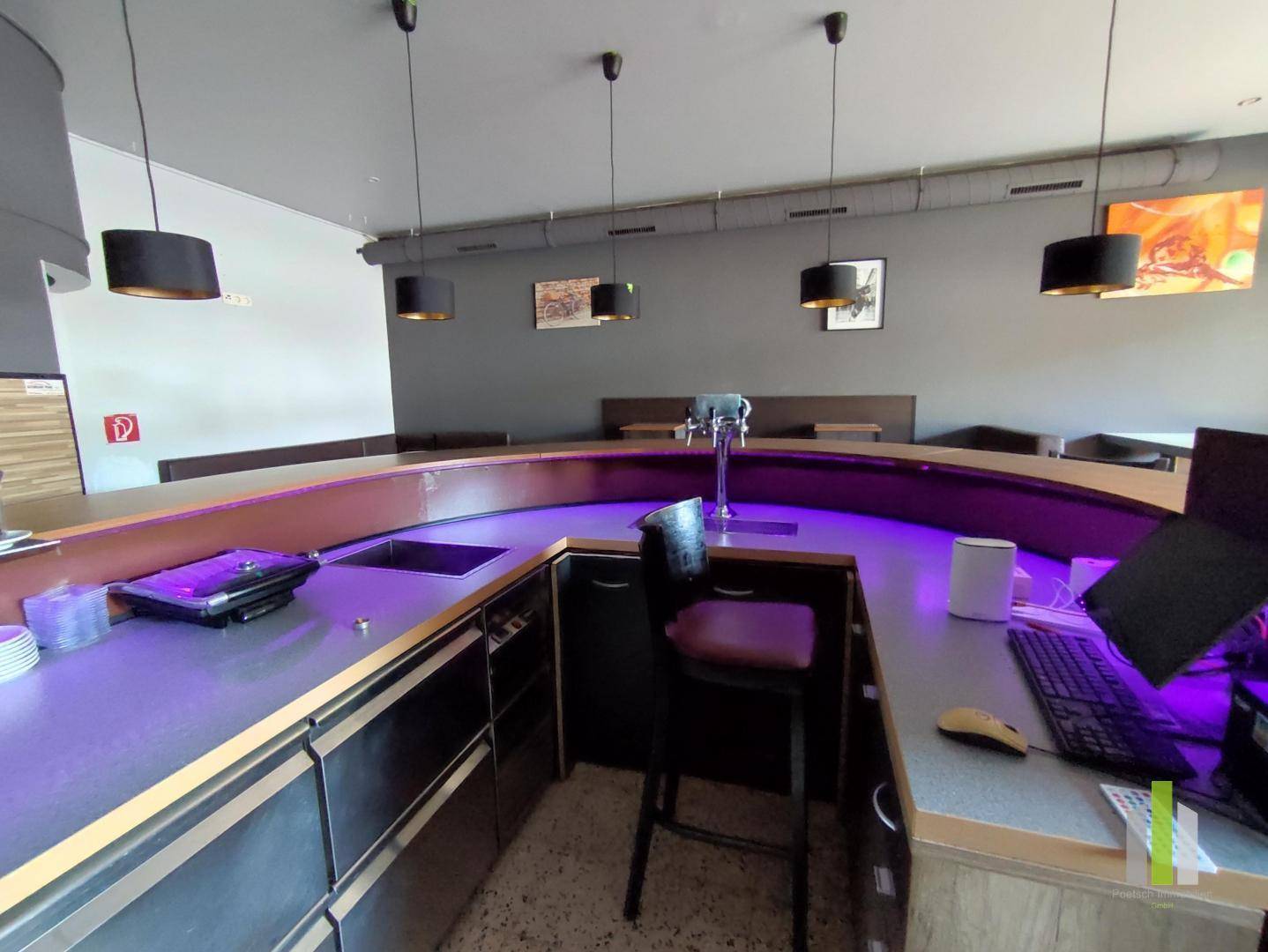 Langer Bartresen mit integriertem Spülbecken und Computerausstattung, beleuchtet von violettem Licht.