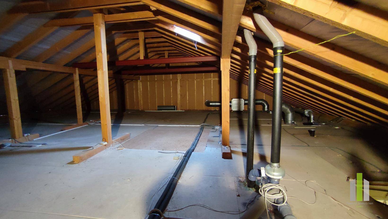 Geräumiger Dachboden mit Holzbalken und Installationsrohren, bietet viel Potenzial.