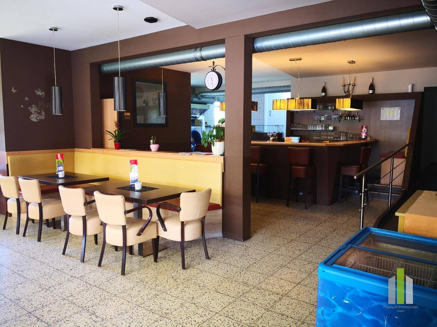 Geräumiger Gastraum mit Sitzbänken, Tischen und einer Bar im Hintergrund, ausgestattet mit Fliesenboden.