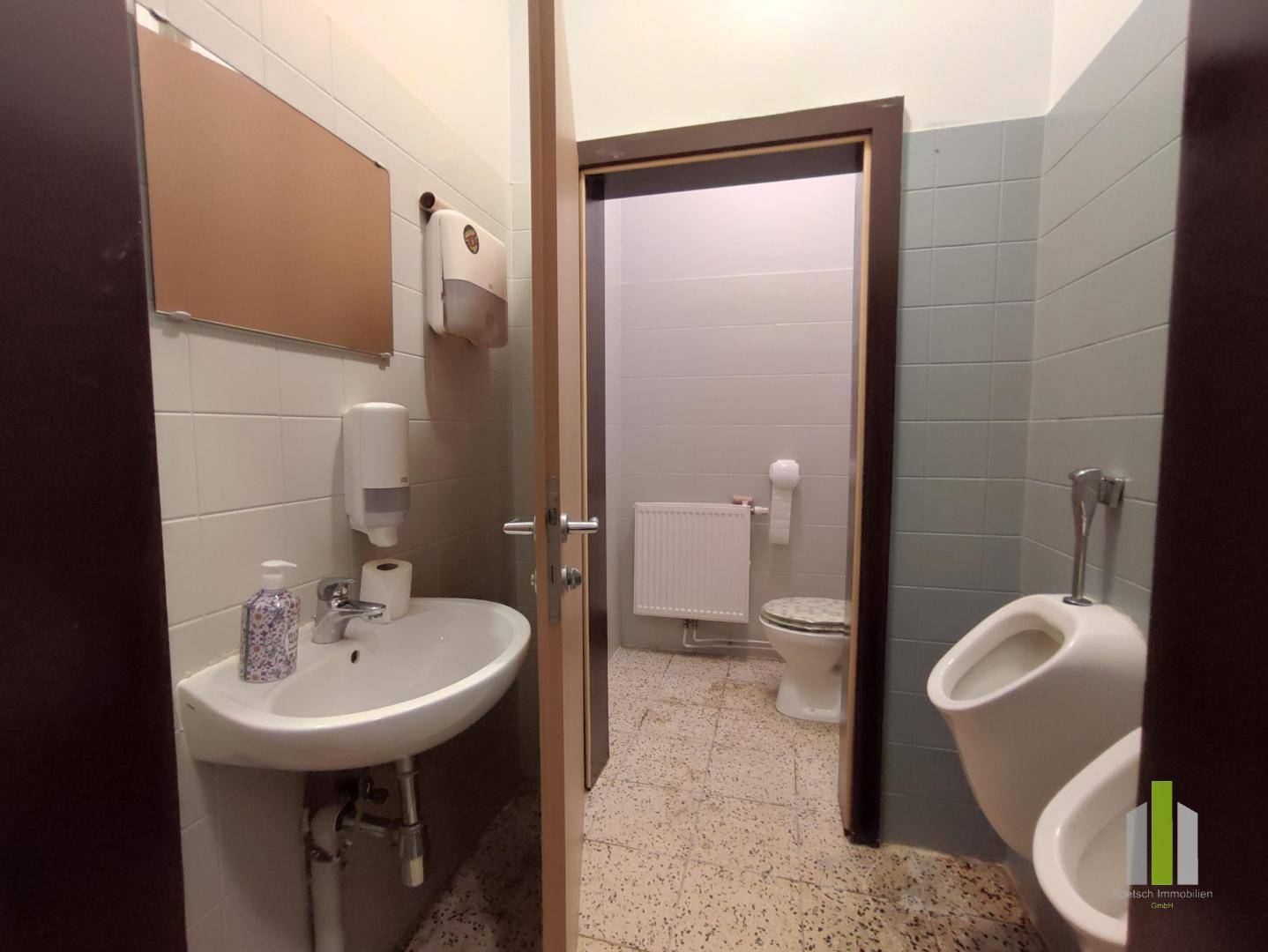 Toilettenraum mit Waschbecken, Spiegel und Urinal, ausgestattet mit Fliesen und Heizkörper.