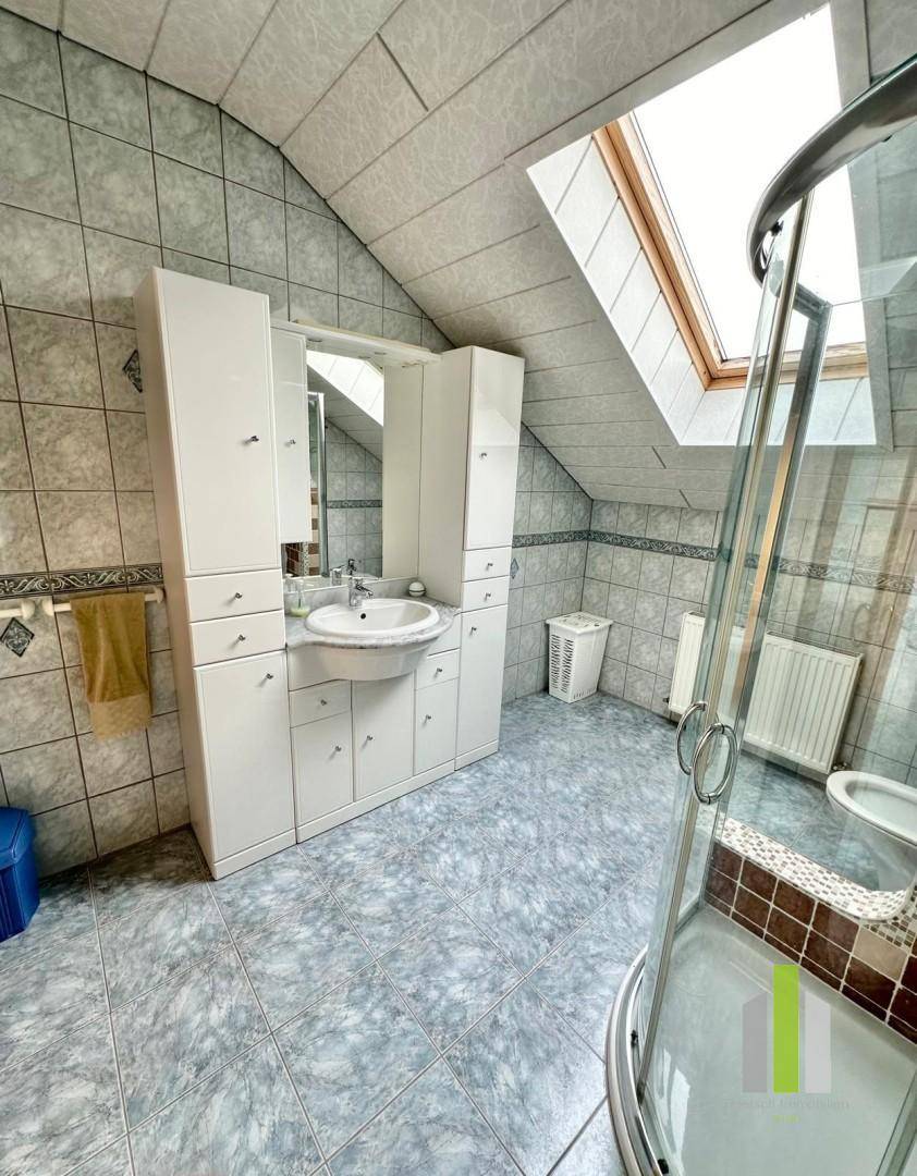 Badezimmer im Dachgeschoss mit Dusche, Dachfenster und hellen Fliesen.