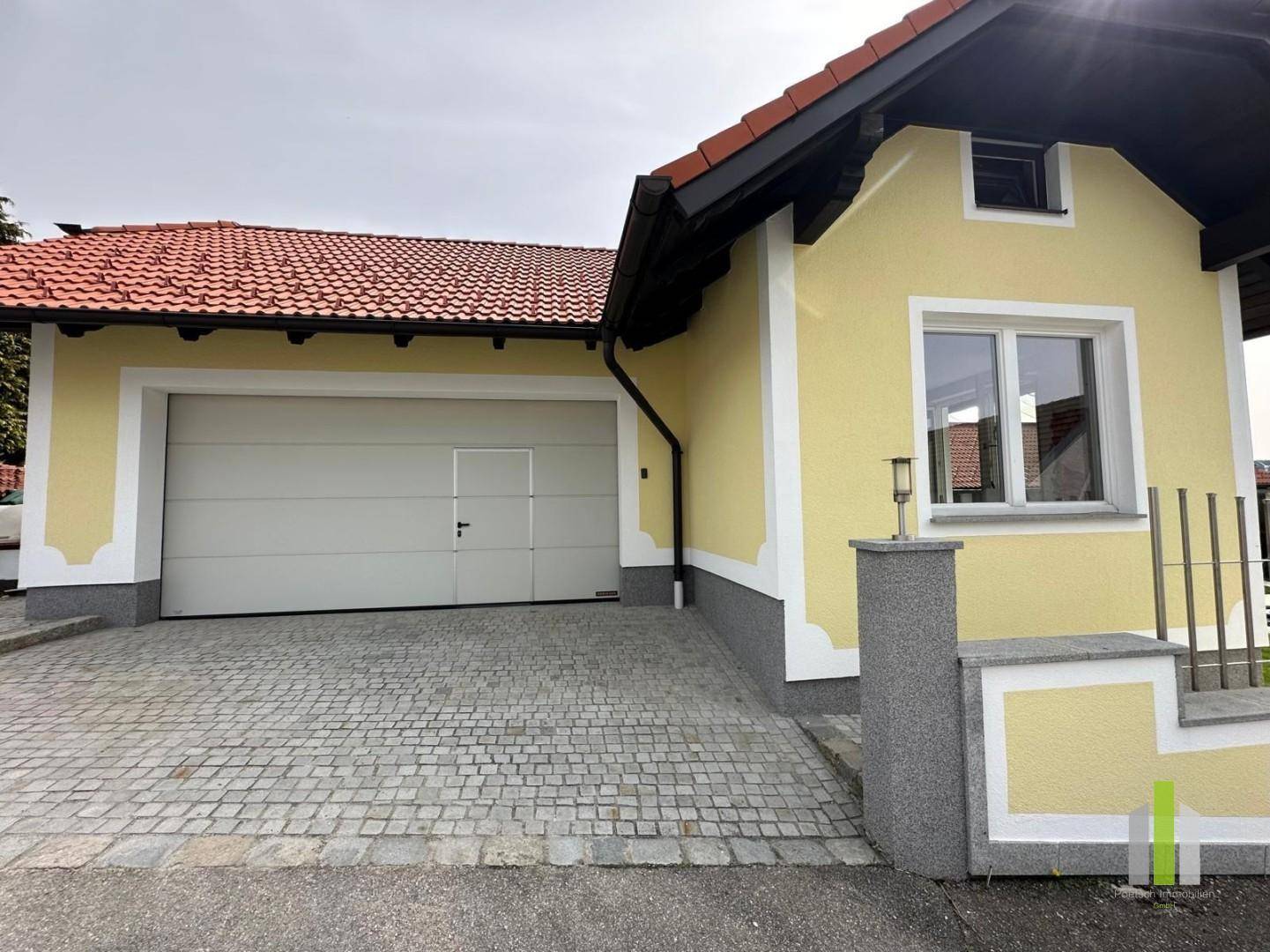 Doppelgarage mit gepflasterter Zufahrt und gelber Fassade des Hauses.