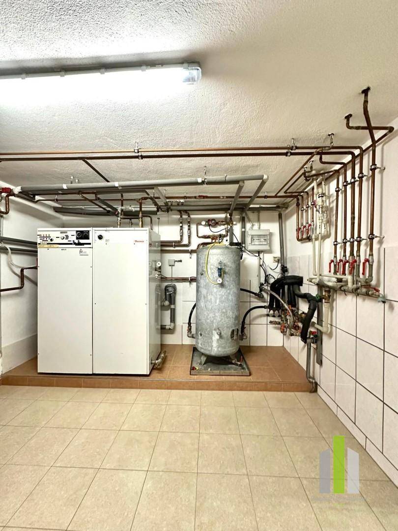 Heizungsraum mit zentraler Heizungsanlage, Warmwasserspeicher und sichtbaren Rohrleitungen.