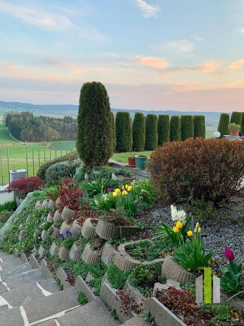 Gestufter Garten mit Blumenbeeten, Steinmauern und weitem Blick über die Landschaft.