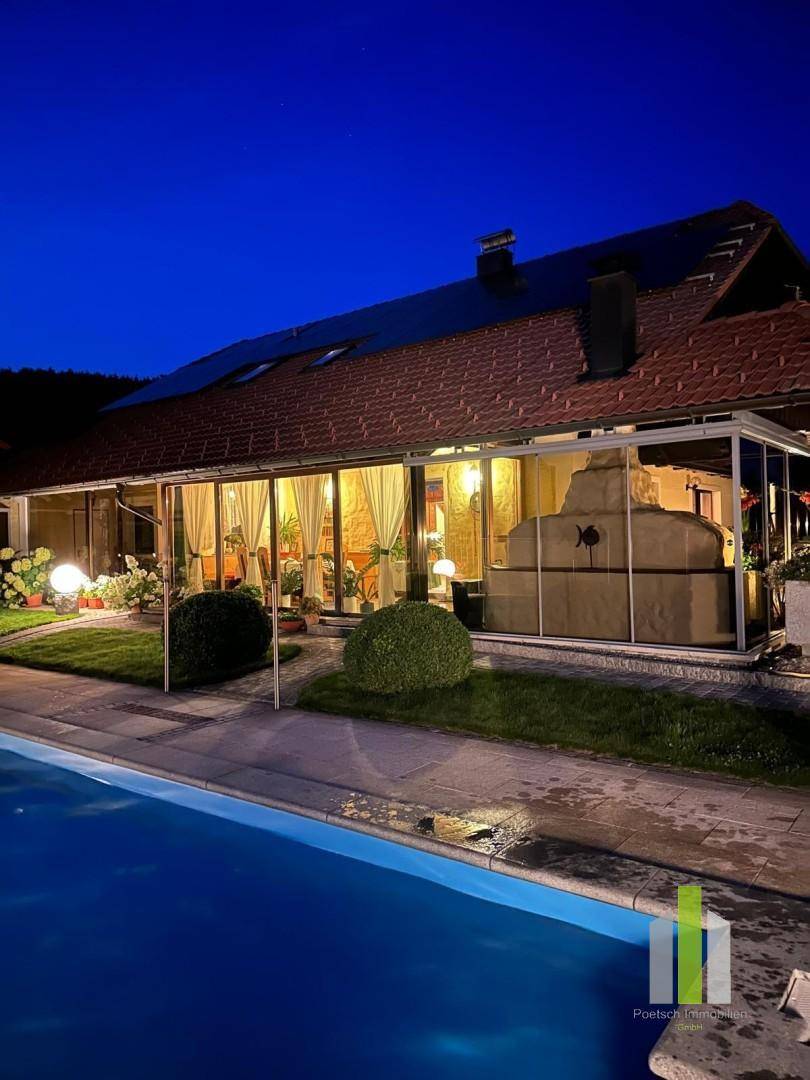 Beleuchteter Außenbereich bei Nacht mit Pool, Liegewiese und gemütlicher Atmosphäre.