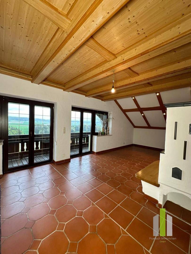 Geräumiger Wohnbereich mit Kachelofen, Terrakottafliesen und Zugang zum Balkon.