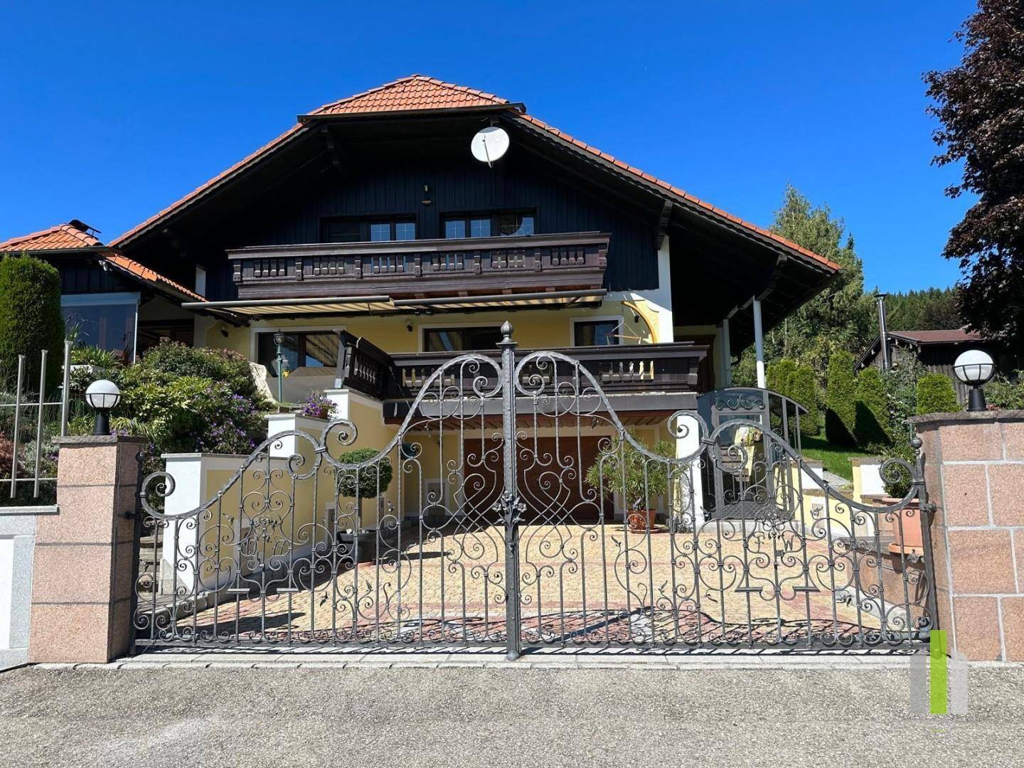 Traditionelles Haus mit schmiedeeisernem Tor und Balkonen in ländlicher Umgebung.