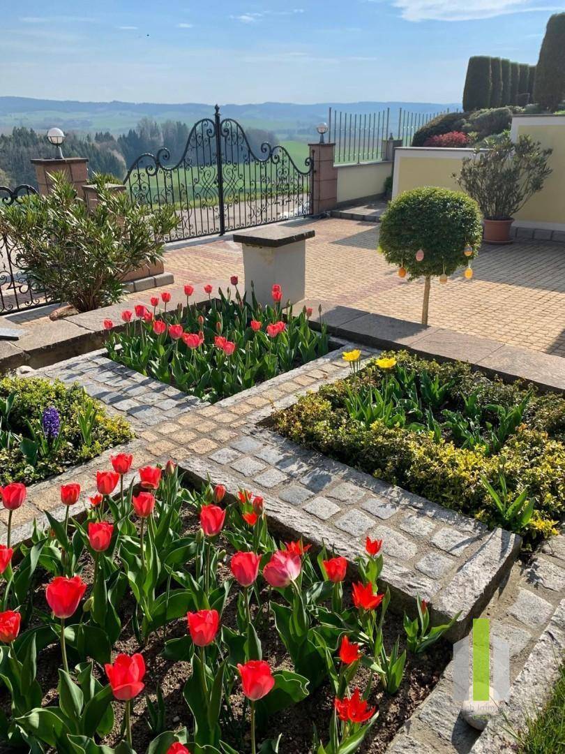 Gepflegter Garten mit bunten Blumenbeeten, gepflastertem Weg und Weitblick.