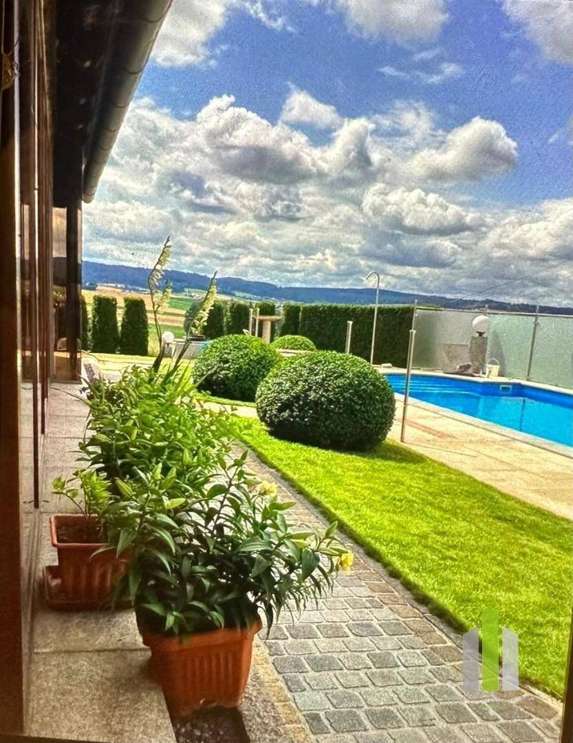 Außenbereich mit Swimmingpool, gepflegtem Rasen und Hecken unter blauem Himmel.