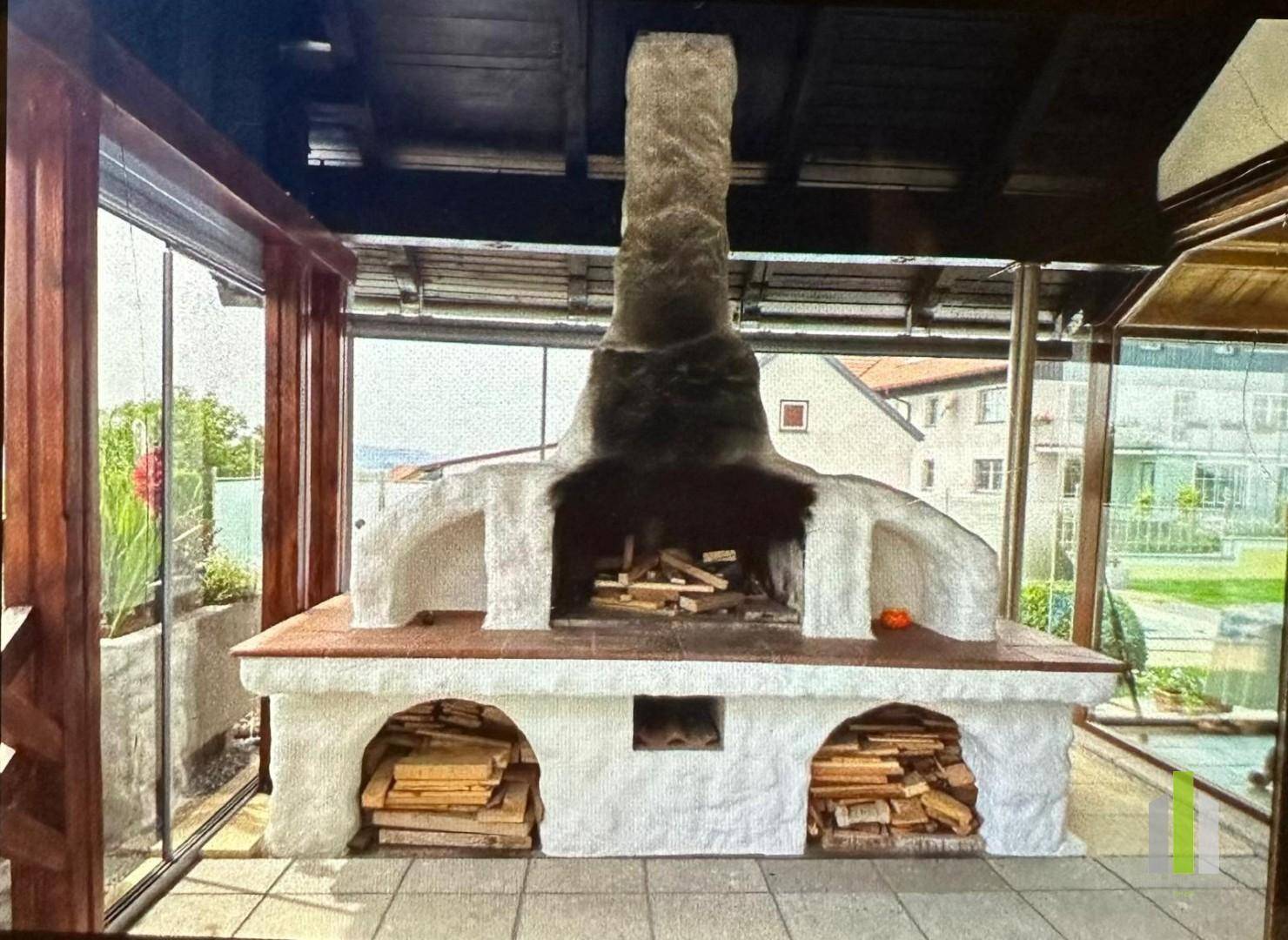 Großer gemauerter Außenkamin mit Holzlager in einem verglasten Anbau.